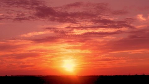Beautiful Dramatic Fiery Sunset over the Horizon in Field in Colorful Sky with Cumulus and Cirrus Clouds, Time Lapse, Slow Motion. Multicolored Red Purple Orange Sky with Clouds and Sun Sets.