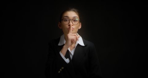 Young businesswoman shows a shh gesture, asks for silence, presses her index finger to her lips, asks for silence. Isolated on a black background