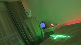 A masked gangster looks menacingly at the camera. Frame for a rap video. A green neon machine illuminates the room.