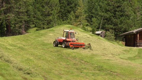 Ortisei, Italy - August 10 2021: Farmer harvesting hay with the tractor on the green pastures in Val Gardena, Italy.