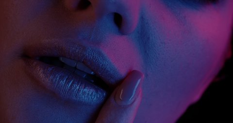 Female lips in neon ultraviolet light. Sexy woman touch her lips with a finger. Shiny lips in a nightclub. Lights and color on a woman mouth. Metallic lipstick.
