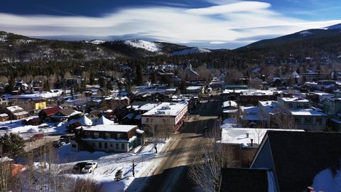 Aerial fasting shot over the main road in Colorado, USA with snow covered mountains in the background and buildings on both sides of road in the foreground.
