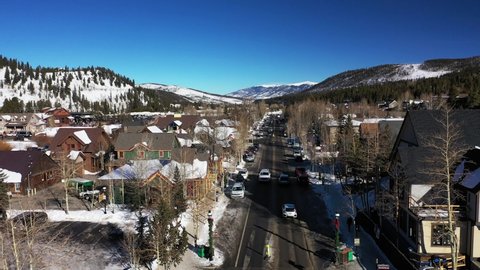 Drone forwarding shot of down main street in Colorado, USA during the winter season. Top aerial of road and sidewalk with people and cars passing by on a cold morning.