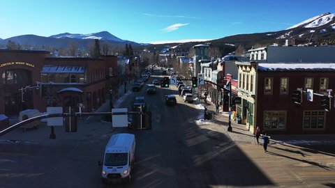 Drone forwarding shot of passing cars on a two way road in the town in foreground and snow capped mountains in the background in Denver, Colorado. USA in the morning.