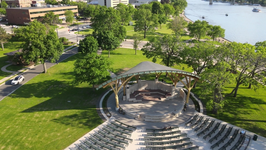Drone view of park venue along Mississippi River in La Crosse, Wisconsin. Timber beams holding roof over stage venue. Benches in semi circle. Sun casting beautiful shadows. 