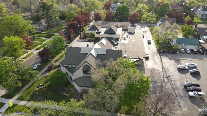 Aerial view of Lutheran church in Wisconsin. Large sprawling building complex on a bright summer day. Tree lined streets throughout the neighborhood. Stained glass windows and cross on roof. 