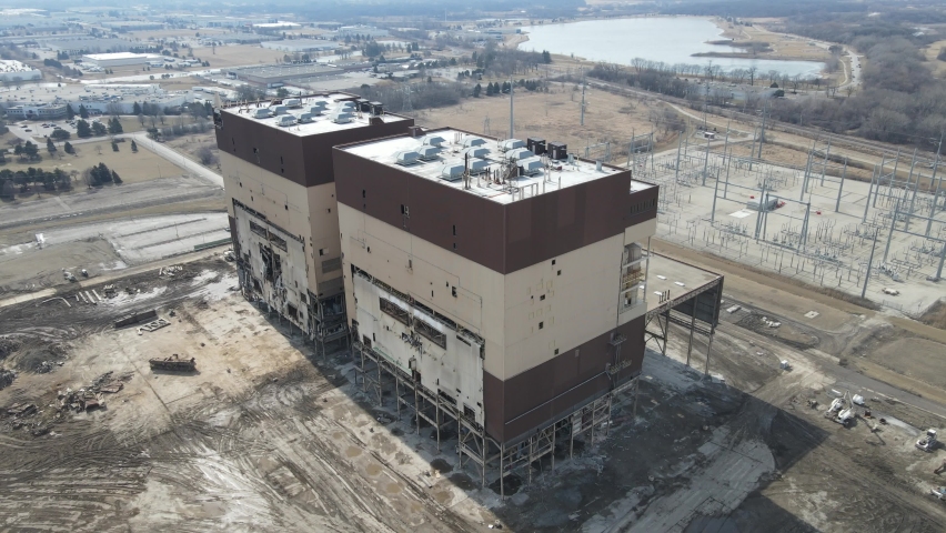 Coal plant being deconstructed from use in Kenosha, Wisconsin. Piles of debris separated out on the site. Lake seen in the distance with sun shining off the water. Hazy blue sky. 