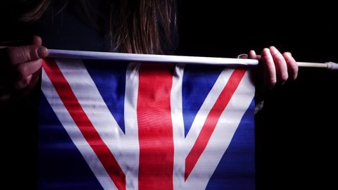 Hand waving British Union Jack flag on dark background medium shot slow motion selective focus