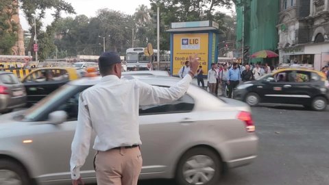 An Indian state traffic police man standing by a roadside managing or guiding the vehicles while pedestrians  waiting to cross the road in a busy metropolitan city, Mumbai, India (January 2020)