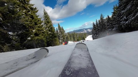 Skiing. Action camera low angle view of skis of skier going downhill on alpine ski on snow slopes in the mountains. Man going downhill on ski having fun on slopes. Winter sport outdoor activity video