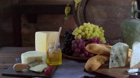 Charcuterie plate board, and wine. Old oak vintage barrel. Cheese pieces, nuts, grapes, honey on a wooden table. Refreshments and tasting alcoholic drinks in the wine cellar.