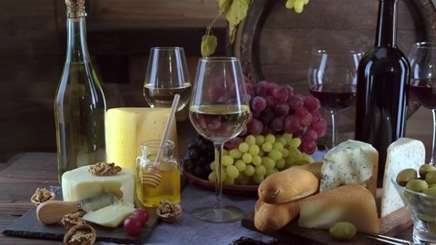 Charcuterie plate board, and wine. Old oak vintage barrel. Cheese pieces, nuts, grapes, honey on a wooden table. Refreshments and tasting alcoholic drinks in the wine cellar.