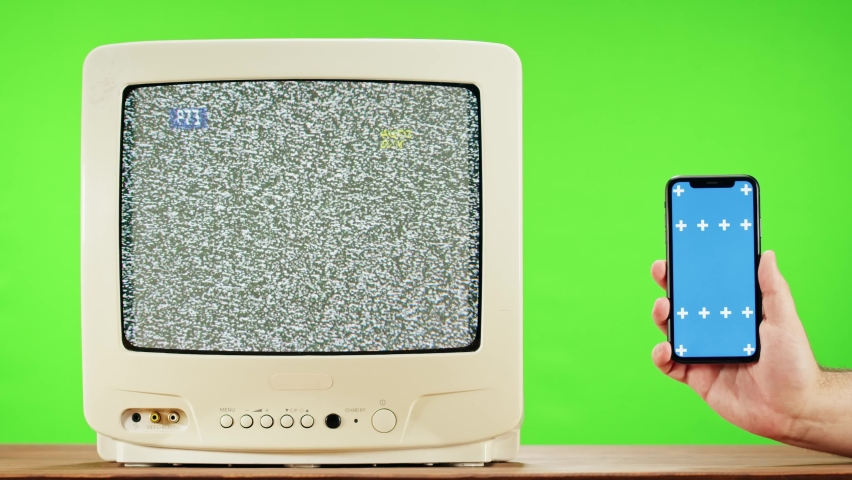 Old television with grey interference screen on green background and smartphone with blue chroma key. Close-up of vintage tv, nostalgia. Gray noise screen and glitches., a Technology Video by volvacheva52