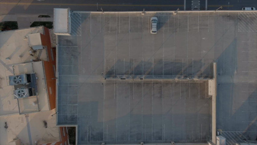 Aerial top-down rising view over building rooftop, parking garage, with parked car in Durham downtown in North Carolina. USA