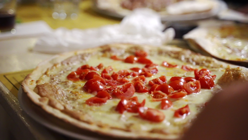 Person turning around white plate with juicy hot round pizza in pizzeria restaurant, Italian pizza with cut fresh tomatoes, pepper and melted mozzarella cheese. Famous homemade pizza Margherita baked