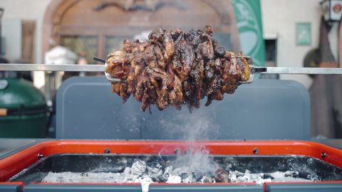 Fat juicy pork rotating on spit and roasting on bbq skewer with pineapple slices inside, tasty meat grilling on burning fire and rising smoke. Preparation of meat delicacy for bbq party, roasting meat