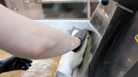 Professional cook is using the special stretching machine for flatting dough at commercial kitchen. Close-up hands works with dough, 4k