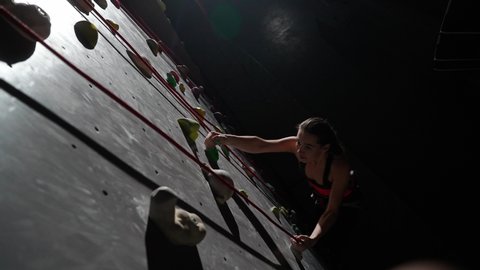 Slow motion, female climber training on a climbing wall, practicing rock-climbing and moving up, climbs the cliff using insurance, cinematic lighting.