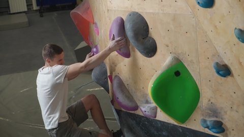 Wellness, climber training on a climbing wall, guy practicing rock-climbing and moving up, 4k slow motion.