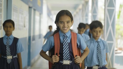 Happy girl kid in uniform standing at school corridor while other kids passing - concept of confidence, education, childhood growth and development.