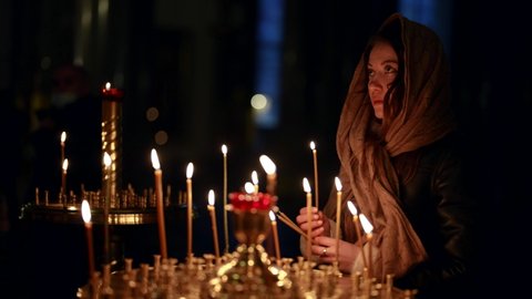 a woman in a headscarf prays in the temple to God in the Orthodox church and puts candles in front of icons