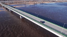 Concrete bridge over burgundy river due to impurities of snow in spring, cars drive across bridge, Drone shooting 4K video, top view