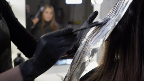 close-up side view of a strand of female hair on a special sheet of foil, the master applies hair dye with a brush. The process of highlighting by a professional master in a beauty salon. Life style