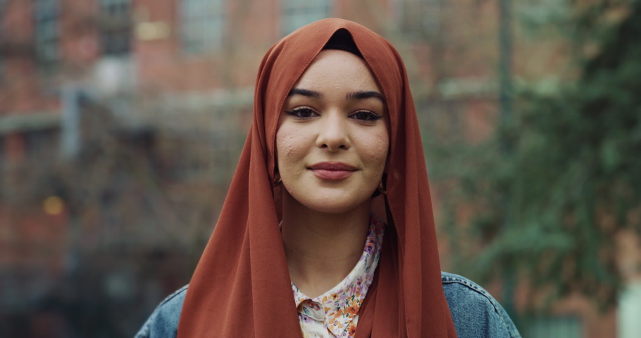 Cinematic shot of young happy Arabian muslim woman is adjusting her hijab and smiling  in camera outdoors. Royalty-Free Stock Footage #1088311415