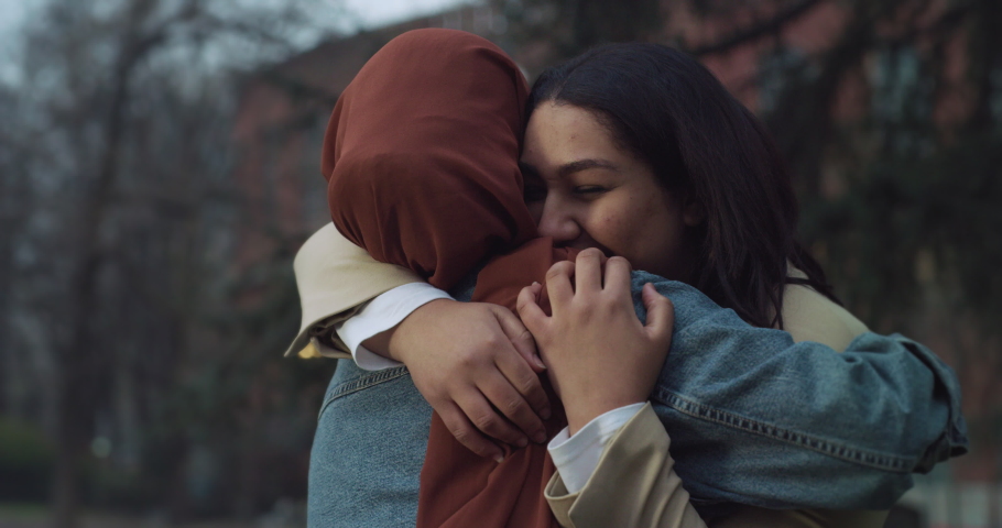 Muslim Hijabi Girl Happily Meet and Hug her Female Friend in a Park. Female Childhood Friends Reunite and Catch Up After Long Years of Distance. Two Multiethnic Women Talk and Laugh