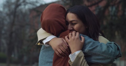 Cinematic shot of young happy Arabian muslim women friends one with hijab and other without are embracing with affection while enjoy to spend time together in green city park.  