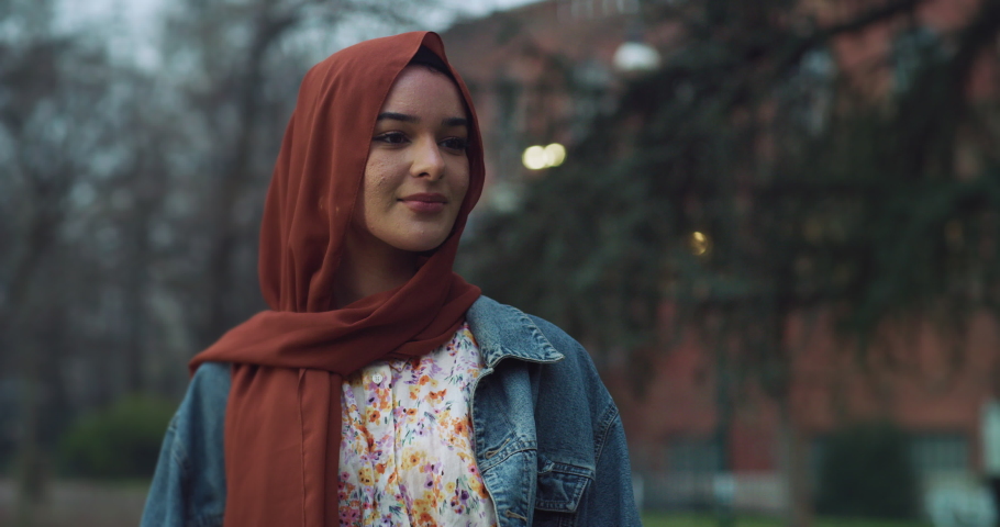 Cinematic shot of young happy Arabian muslim women friends one with hijab and other without are embracing with peace sign rainbow flag in green city park.