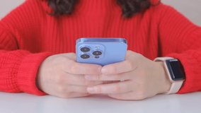 Girl typing message on mobile phone. Young white woman in red sweater using modern blue smartphone for communication online. 4k stock video of female person writing comment on social media app