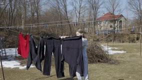 A woman carefully hangs her laundry in the backyard of her house. Housekeeping, the work of a woman.