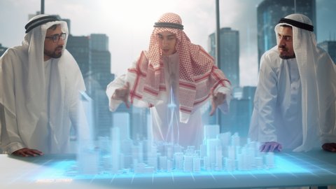 Group of Arab Real Estate Business Developers in Traditional Clothes Discuss Investing Opportunities Based on Holographic Augmented Reality 3D City Model in Their Modern Office in a Skyscraper.