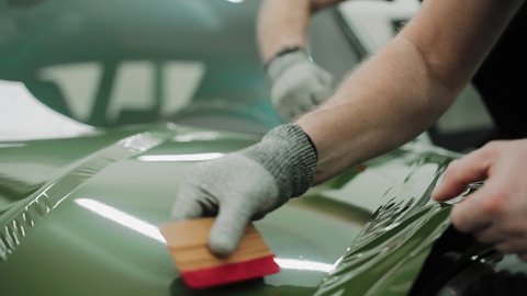 Process of vinyl wrapping a car hood in dark green color using plastic cards. Process of vinyl wrapping a car hood in a car studio. Shiny khaki green car vinyl wrap. High quality 4k footage