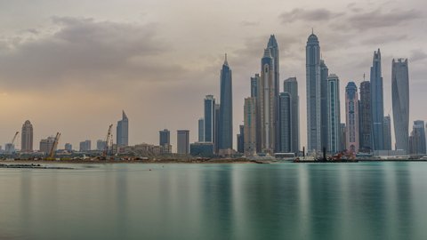 Panorama of modern skyscrapers in Dubai city at sunrise timelapse from the Palm Jumeirah Island. Dubai, United Arab Emirates. Dubai marina in clouds at early morning
