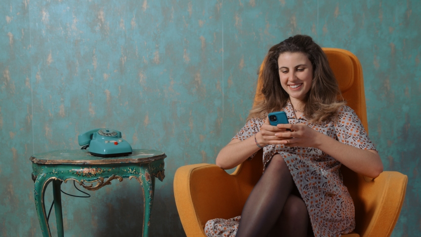 retro and new technology-woman sitting near an old rotary phone uses cellphone