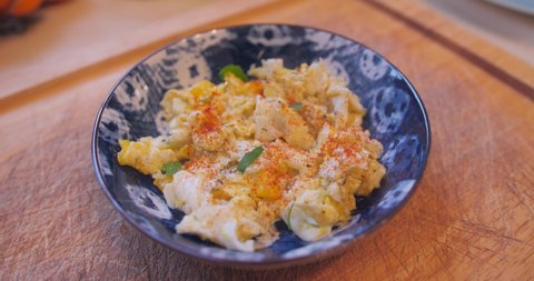 Close up view of Scrambled eggs with paprika and parsley in a blue bowl on a kitchen table.