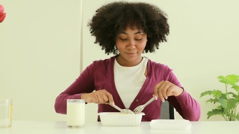 Portrait of an African-American teenage girl eating rice and fried eggs in a plastic container bought at a supermarket with a scoop of rice, shows how happy she is.