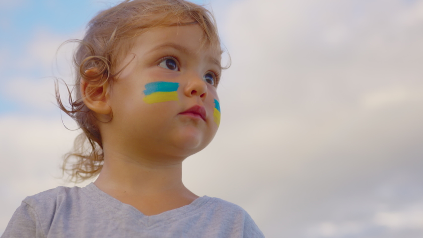 Close up portrait little baby with flag of Ukraine on face sitting alone. Protest against Russian war invasion in Ukraine. Ukrainian Flag, Protesters concept | Shutterstock HD Video #1088328011