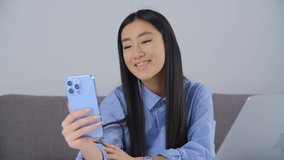Vietnamese girl talking on video call. Cute young southeast asian female speaking frontal camera of modern blue mobile phone with triple camera connected to fast internet. BIPOC person lifestyle clip
