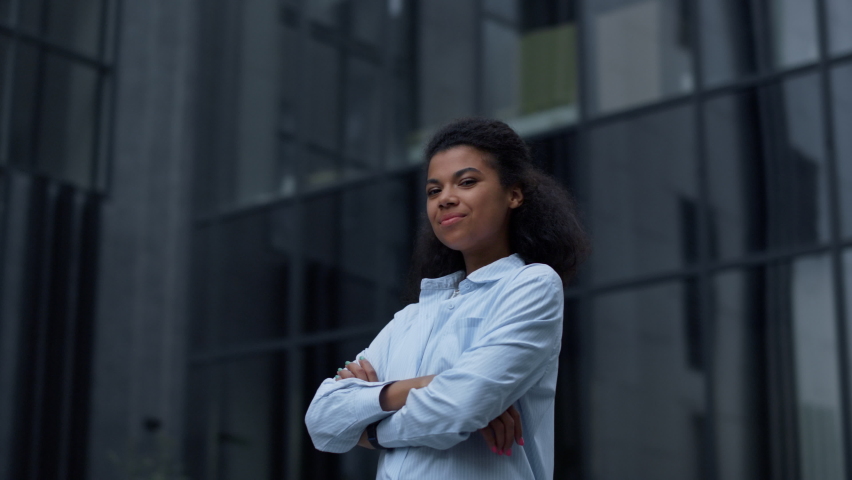 Satisfied manager standing at office building. Proud happy woman look in camera. Relaxed attractive girl businesswoman enjoying triumph moment. Successful african american woman get job promotion. Royalty-Free Stock Footage #1088329339