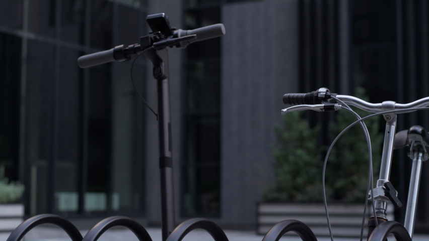 Closeup electric scooter standing at shared parking together with black bicycle. Modern two-wheeled eco-friendly vehicles waiting for rider on empty city street. Urban traveling equipment concept.