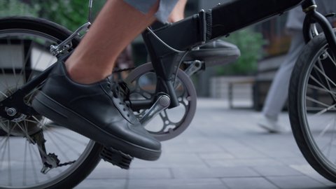 Closeup male legs pedaling city street in black shoes. Unrecognized man startup ceo riding bicycle commuting to work on eco-friendly transport. Successful assistant worker enjoy downtown trip on bike