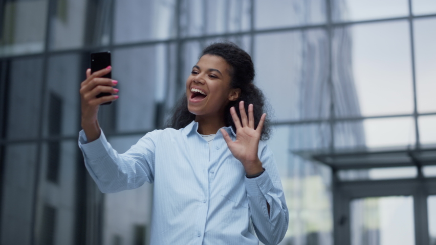 Happy woman making online video call talking with friend. Joyful communication. Attractive African American girl share good news on virtual conference at modern office building. Wireless technologies.
