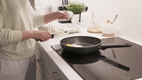 Woman cooking scrambled eggs on electric stove top in the kitchen, frying pan with fried eggs on induction cooktop closeup. High quality 4k footage