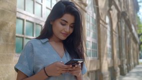 A young Modern happy Indian Asian hipster modern stylish female or woman is standing outdoors against an old vintage downtown building and chatting or typing a text message on a Mobile phone.  - Powered by Shutterstock - Get 15% off with code: PIKWIZARD15