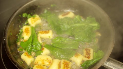 gnocchi with spinach greens and green peas is cooked in a frying pan close-up top view video