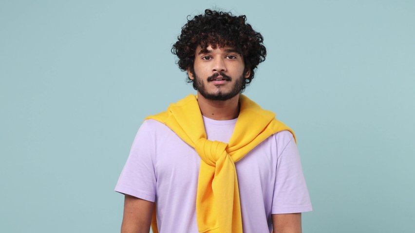 Happy cheery young bearded Indian man 20s wears violet t-shirt look around for friend find waving meet greet with hand as notices someone isolated on plain pastel light blue background studio portrait Royalty-Free Stock Footage #1088333501