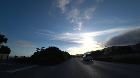 OKINAWA, JAPAN - AUGUST 2021 : Driving shot of Okinawa in sunset time. Point of view (POV), seaside road drive. Summer holiday, vacation and travel concept video.